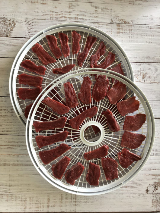 Thin slices of lean bison meat on dehydrator racks for making bison pemmican.